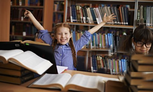 Excited little girl doing research at the library together with her friend